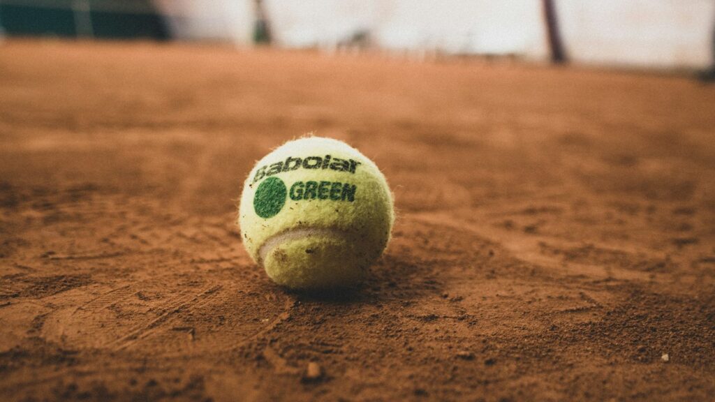 Balle de tennis verte d'initiation posée sur la terre battue