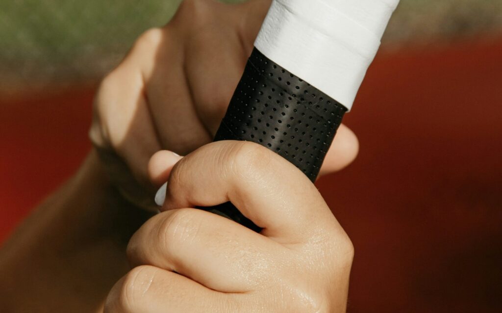 Mains tenant le manche d'une raquette avec un surgrip blanc